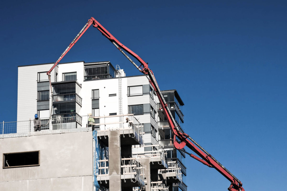 Huge concrete pump with tall arm pumping conrete on top of the building with unrecognizeable workes