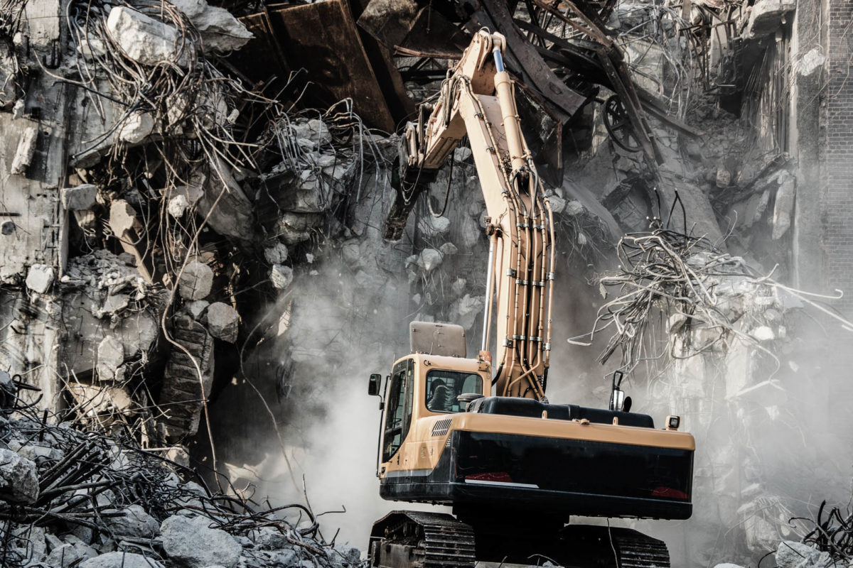 Excavator working at the demolition of an old industrial buildin Excavator working at the demolition of an old industrial building.